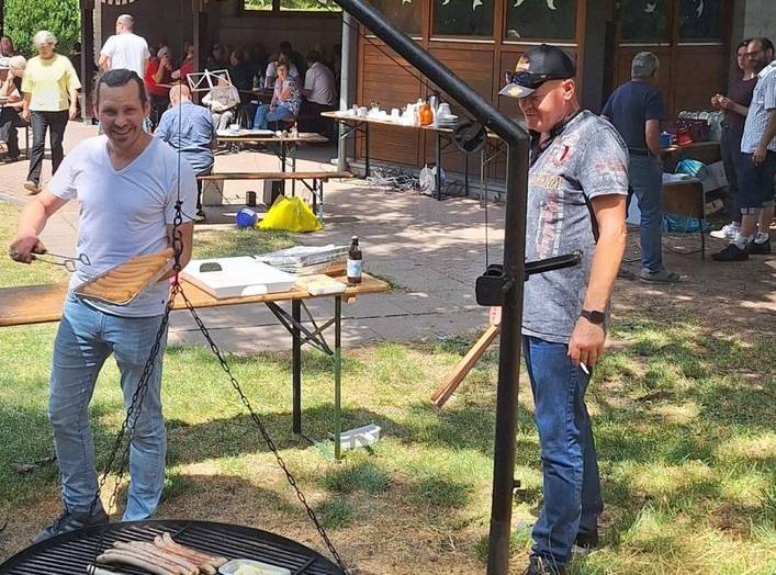 Sommerfest 2025 Begleitetes Wohnen in Familien (BWF) –  Zwei Personen stehen neben einem großen Grill.   