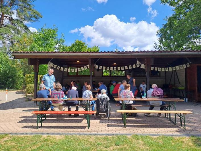 Sommerfest 2025 Begleitetes Wohnen in Familien (BWF) – Personen sitzen im Pavillon und im Freien davor.